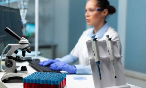 Biologist researcher woman with white coat discovering vaccine against virus typing medical expertise on computer. Professional modern equipment standing on table in hospital laboratory